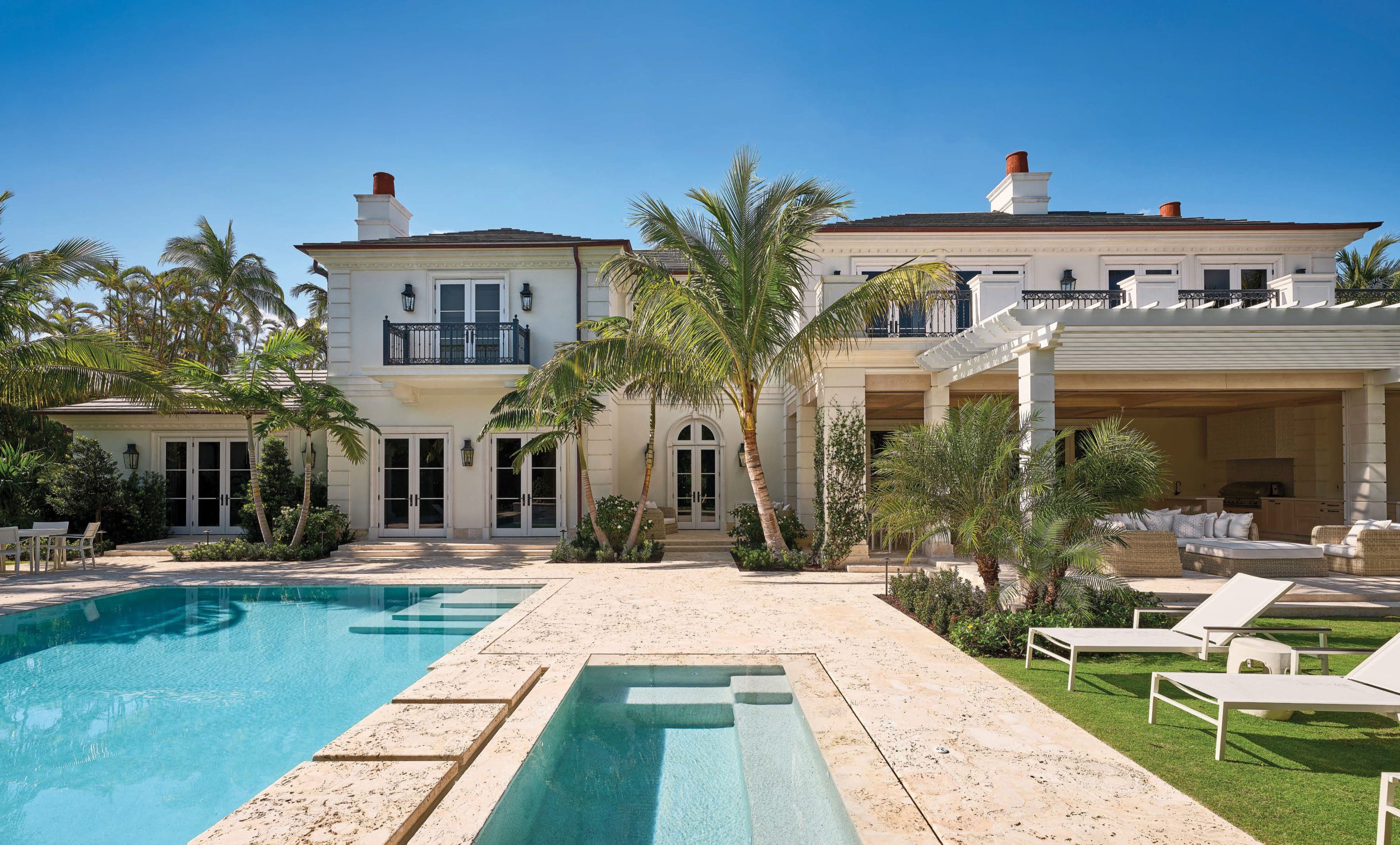 The rear garden of a Phipps Estates residence in Palm Beach, with a coquina-edged pool and spa, palms, and a loggia behind