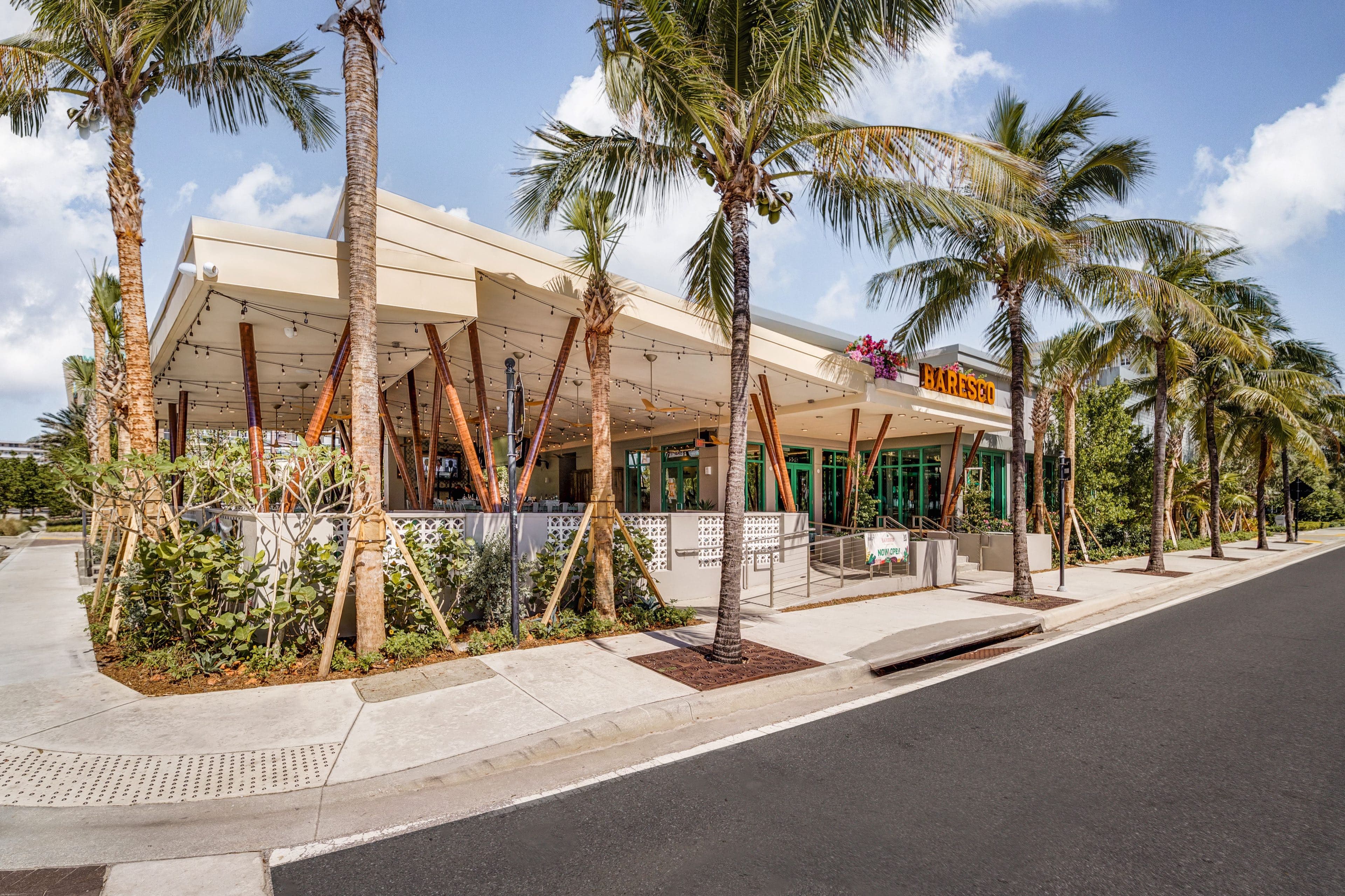 The Baresco restaurant beneath its angled white canopy, fronted by a row of coconut palms in planted beds along the street